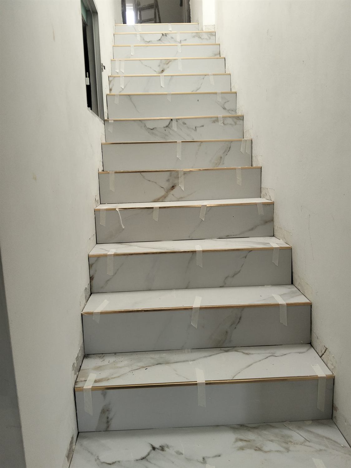Escalera revestida en porcelánico efecto mármol con perfil dorado en cada peldaño